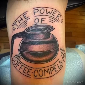 Фото тату на руке с изображением кофеварки и надписью 'THE POWER OF COFFEE COMPELS ME'. Черно-белая татуировка, реалистичный стиль.