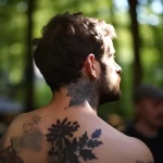 Фото тату: черно-серая татуировка с изображением растения на шее и верхней части спины. Детализированный рисунок с использованием тонких линий.