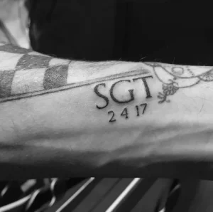 Черно-белое фото татуировки на предплечье с надписью 'SGT' и датой '2417'. Простой, лаконичный дизайн, символизирующий военную службу.