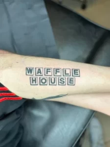 Фото тату: на предплечье мужчины нанесена простая татуировка надписью 'WAFFLE HOUSE' черным цветом, выполненная в стиле минимализм.