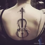 Фото тату виолончели на женской спине, выполненное в черном цвете с детальной проработкой и легкими брызгами краски. Идеальный эскиз тату для музыкантов.