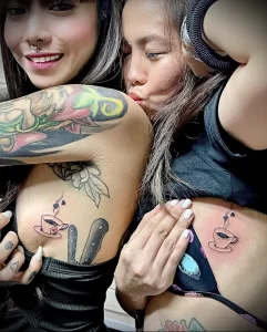 Фотография двух девушек с небольшими татуировками на груди: чашка кофе с сердцем и нож. Символизирует любовь к кофе и дерзость.