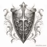 Черно-белый эскиз татуировки с изображением щита, украшенного крестом и витиеватым орнаментом. Детализированный рисунок, выполненный карандашом, подходит для любителей истории и геральдики.