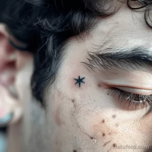 Фотография маленькой татуировки в виде звезды, расположенной у глаза мужчины. Простой и стильный рисунок, выполненный в черном цвете. Идеальный эскиз для минималистичной тату.