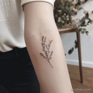 Фото тату: тонкая веточка с небольшими цветами, выполненная в технике line work, расположена на руке. Минималистичный и женственный рисунок татуировки.