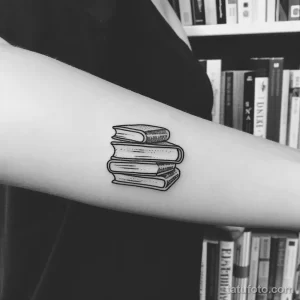 Черно-белое фото тату с изображением стопки книг на предплечье. Минималистичный стиль, графичный дизайн, идеально для любителей чтения и литературы.