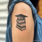 Фото тату: реалистичное изображение книги с академической шапкой на руке девушки. Черно-белый рисунок татуировки с детальной проработкой.