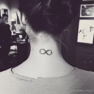 Фото тату маленького символа бесконечности на затылке девушки. Изящный рисунок татуировки черного цвета, выполненный тонкими линиями.