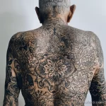 Фото тату: масштабная татуировка в виде цветочного орнамента, покрывающая всю спину и шею мужчины. Детализированный рисунок татуировки.