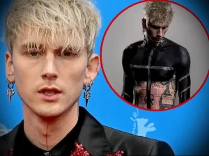 Фото крупным планом лица и верхней части тела Machine Gun Kelly, демонстрирующее его татуировки, включая надпись на шее и рисунки на груди и руках.