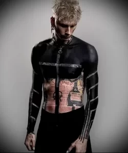 Фотография музыканта Machine Gun Kelly с обширными татуировками на теле, одетым в черную одежду.
