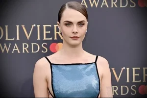 Фото знаменитости: Cara Delevingne на красной дорожке в голубом платье, демонстрирующая татуировку на плече.