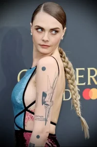 Фото тату с изображением абстрактного портрета и надписи на плече Cara Delevingne, для вдохновения на создание уникального и художественного дизайна.