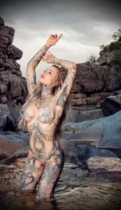 Фотография девушки с обилием татуировок на теле, стоящей в воде на фоне скал. Идеально для демонстрации татуировок в естественной среде.