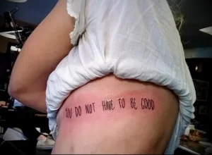 Фото минималистичной татуировки надписью 'You do not have to be good' на боку девушки. Подробное изображение для поиска идей.