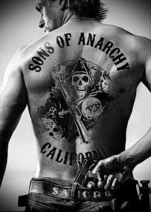 Фото тату на спине мужчины, изображающее логотип байкерского клуба Sons of Anarchy с черепом и надписью California. Татуировка выполнена в черно-белых тонах.
