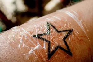 Фото свежей татуировки в виде звезды, покрытой защитной пленкой. Видны небольшие покраснения и отек вокруг татуировки.