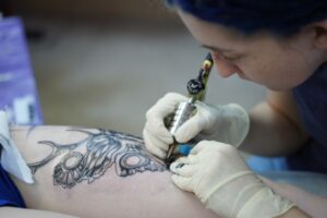 Фото процесса нанесения татуировки опытным мастером. Виден аппарат для тату, рука клиента и сосредоточенное выражение лица тату-художника.