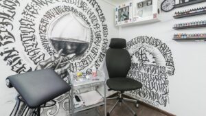 Фото интерьера тату-студии, оформленной в стиле Blackwork. Черно-белые рисунки на стенах, удобное кресло и профессиональное оборудование.