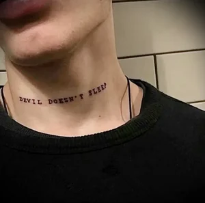 Черная надпись татуировка на шее: 'Devil Doesn't Sleep'. Минималистичный шрифт, расположенный вдоль линии шеи.