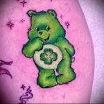 Фото яркой татуировки на руке: зеленый медвежонок Care Bear с четырехлистным клевером.