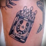 Фото тату коробки спичек с подковой внутри и надписью 'Luck'. Черно-белый рисунок в стиле графика с детализированной проработкой.