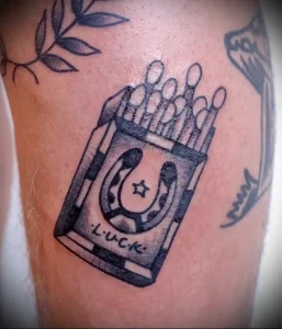 Фото тату коробки спичек с подковой внутри и надписью 'Luck'. Черно-белый рисунок в стиле графика с детализированной проработкой.