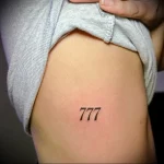 Фото минималистичной татуировки на боку: число 777. Черно-белый рисунок татуировки.