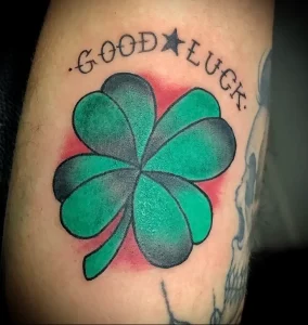 Фото яркой татуировки на руке: четырехлистный клевер с надписью 'GOOD LUCK' и звездой. Цветной рисунок татуировки.