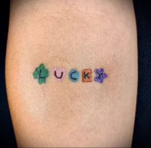 Фото тату: оригинальная татуировка надписи "LUCKY", выполненная в стиле патчворк с использованием разных цветов и текстур на руке.