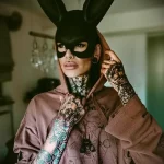 Фото тату: девушка в маске зайца с татуировками на руках и шее. Темные и загадочные рисунки с использованием геометрических фигур и насекомых.