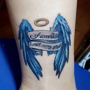 Фото тату: татуировка крыльев голубого цвета с нимбом и надписью "Farrell I still carry you" на лодыжке. Эскиз татуировки в стиле акварель.