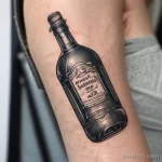 Фото тату бутылки Jack Daniel's на руке. Черно-белый рисунок татуировки выполнен в реалистичном стиле с проработкой деталей.