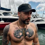 rugged man with an anchor tattoo on his wrist, symbolizing steadiness, standing by a harbor tattoo lion, on neck sexy girl, phot tatufoto.com 243