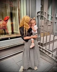 Фотография женщины, обнимающей маленькую девочку на улице. Женщина в длинном платье, девочка в светлом наряде.