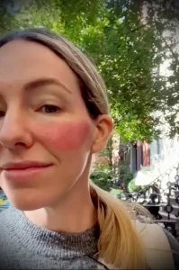 Фото тату на щеке девушки: небольшая татуировка, выполненная в нежных тонах. Минималистичный дизайн, оригинальный стиль. Часть татуировки переходит на волосы.