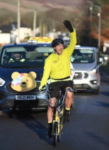 Фото Paddy McGuinness на велосипеде во время благотворительного забега Children in Need. Видны татуировки на руках велосипедиста. Подчеркивает энергию и целеустремленность.