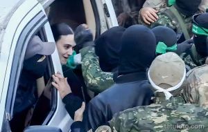 Фотография мужчины с татуировками, окруженного людьми в масках и военной форме, демонстрирующая напряжение и защиту.