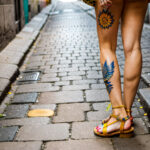 Как вес влияет на тату A petite woman with a colorful bird tattoo on her ankle walking along a cobblestone street wearing summer sandals medium-leng tatufoto.com 168