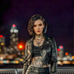 Как вес влияет на тату A slender woman with a blackwork sleeve tattoo standing by a city skyline at dusk wearing a fitted leather jacket short dark tatufoto.com 139