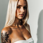 Как вес влияет на тату A tall woman with a minimalist line art tattoo on her collarbone standing in a photo studio wearing a strapless top long stra tatufoto.com 162