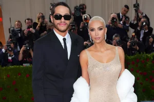 Фотография Ким Кардашьян и Пита Дэвидсона на красной дорожке Met Gala. Ким в блестящем платье, Пит в черном костюме и темных очках.