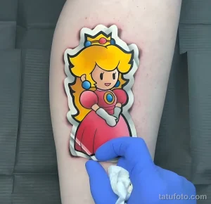 Фото тату с изображением принцессы Пич из игры Super Mario Bros на руке. Яркие цвета и милый образ персонажа.