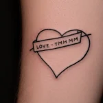 Черно-белое фото татуировки сердца с надписью "LOVE" на запястье, выполненной простым шрифтом.