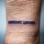 Черно-белое фото татуировки надписи на запястье, выполненной простым шрифтом.