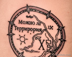 Фотография татуировки на коже, изображающей компас с надписью "Можно ли Территория" и различными символами внутри.