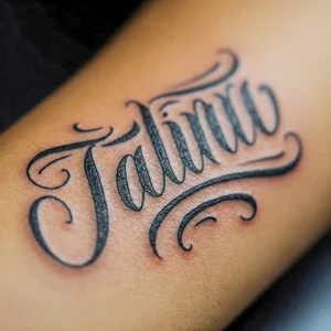 Фото тату с красивой надписью 'Jalina' выполненной каллиграфическим шрифтом на предплечье. Черные чернила, плавные линии.