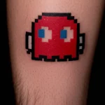 Фото тату пиксельного призрака Pac-Man. Цветная татуировка на предплечье, выполненная в стиле 8-bit графики.