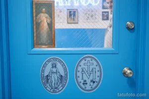 Фото двери тату-студии с изображением религиозной фрески и символов веры, таких как Дева Мария и крест.