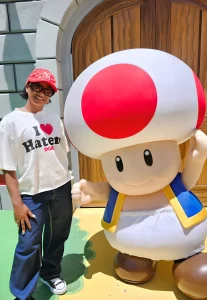 Фотография человека рядом с большим персонажем Тоада из Super Mario. Акцент на ярких цветах и необычном образе.